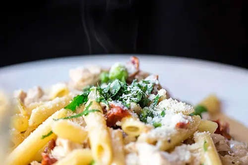Steaming hot alfredo pasta on a white plate