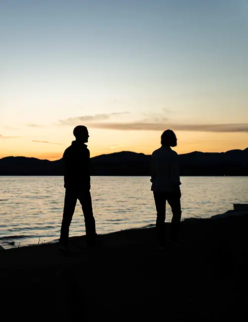 Silhouette of two people walking by the water and sunset