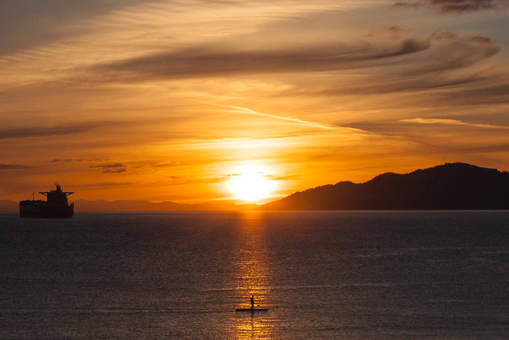 Paddleboarder in the spotlight of the sunset in the water