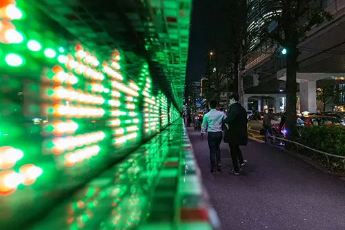 Two people walking by a bright green LED sign